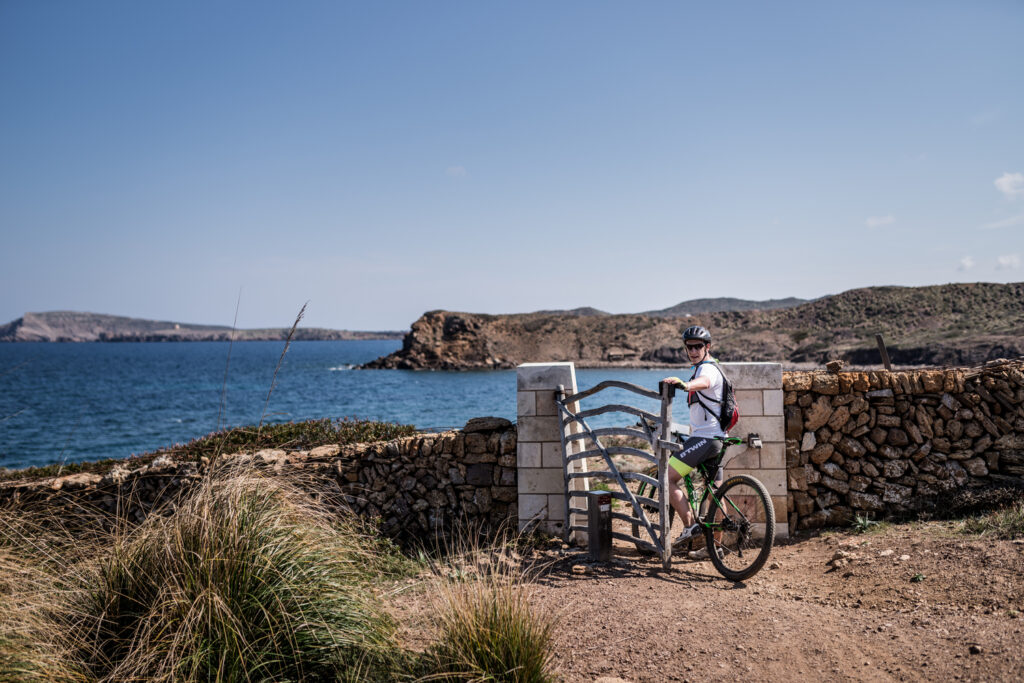 Un ciclista obrint una de les moltes barreres que hi ha al Camí de Cavalls (Foto: The Adventure Bakery).